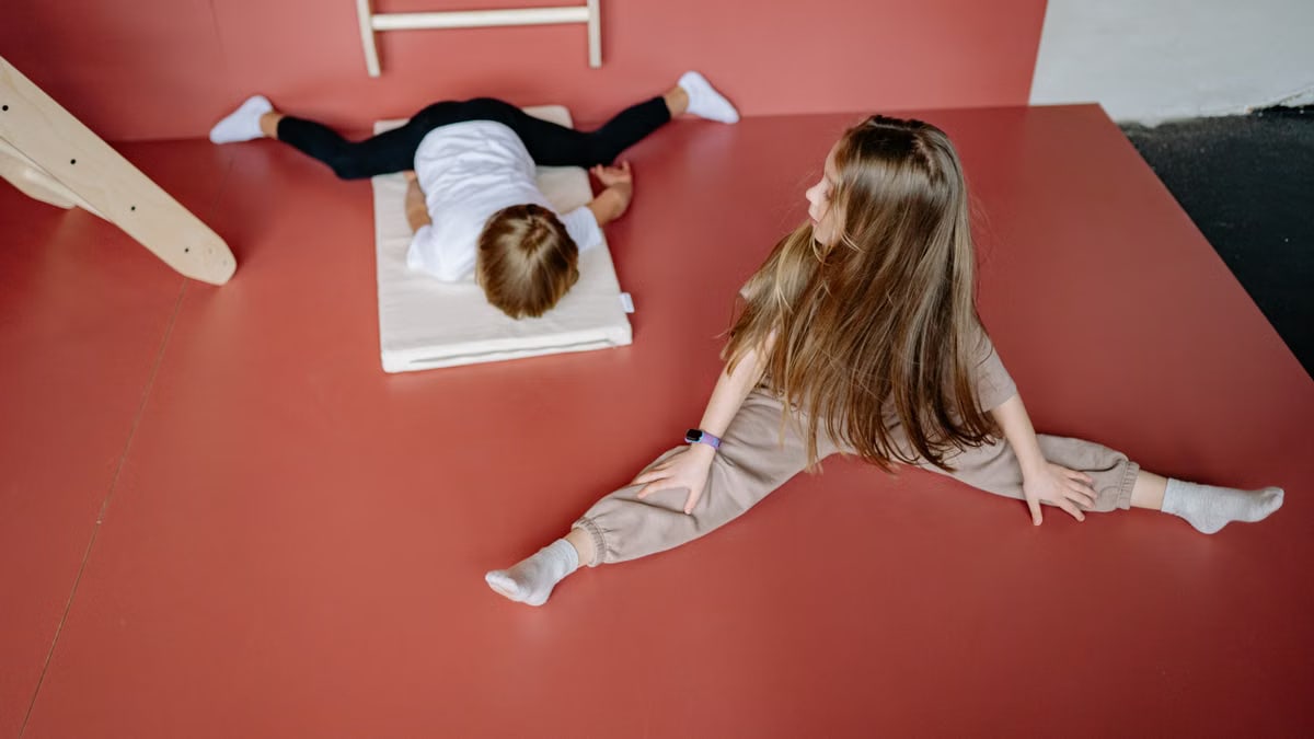 Two children engaging in gymnastics on a mat indoors, showcasing flexibility and playfulness.